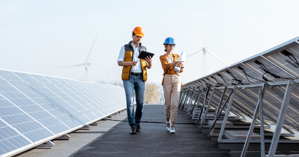 Frau und Mann gehen zwischen zwei Reihen von aufgeständerten Solarmodulen entlang